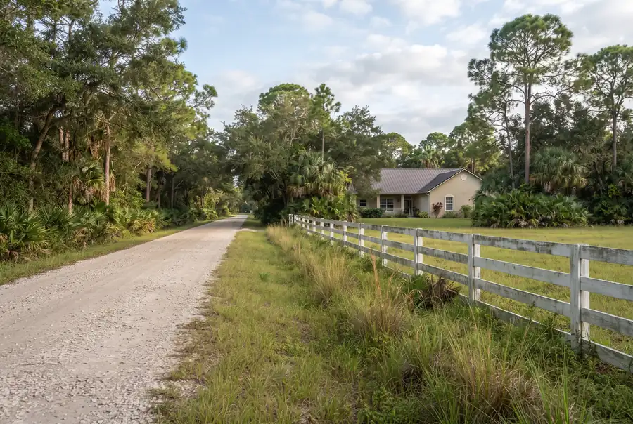 Quiet rural residential road with wide lots, tall pines and a white rail fence in The Acreage, Florida